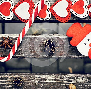 Funny outdoor Christmas composition with pine cones, lollipop, acorn, star anise, snowman and colorful felt hearts on an old