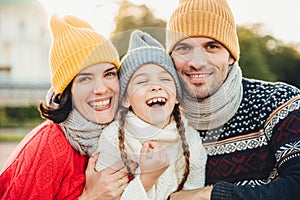 Funny overjoyed small kid laughs as has wonderful time with her parents. Affectionate parents stand near their little daughter who