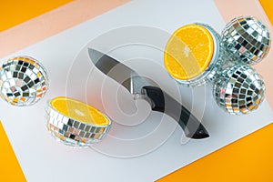 Funny party. Disco balls and mirror cut ball with orange fruit inside. Top view, flat lay. Kitchen knife and orange cut