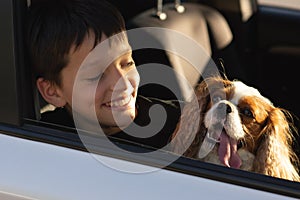 Funny photo of teenager boy smiling looking out car window with his dog cavalier king charles spaniel, about to go on a trip