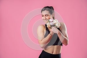 Funny photo of a young muscular fitness girl with a bouquet in her hands, that sniffs flowers and pumps up muscles. Cheerfully
