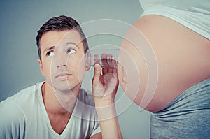 Funny photograph of a dad holding a glass to the belly of his wife