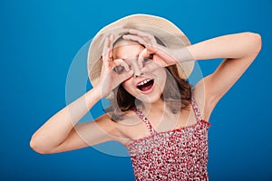 Funny playful little girl in hat making glasses by hands