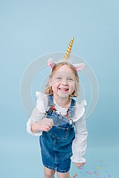 Funny playful little girl in unicorn head band over blue background
