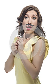 Funny Playful Portrait of Smiling Happy Laughing Caucasian Brunette Girl in Posing with Artificial Moustache in Yellow Dress Over