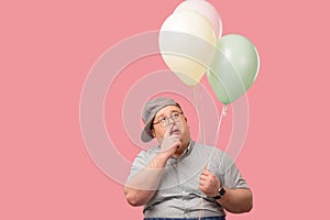 Funny plump guy standing with air balloons having doubts isoated on pink