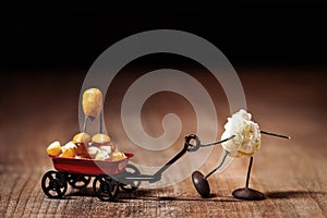 Funny popcorn figure is moving a handcart with a corn figure