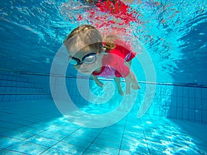 Funny portrait of baby girl swimming and diving in blue pool