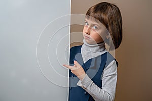 Funny portrait of beautiful serious young girl looking behind white empty banner. Free copy space for text or design. Horizontal
