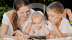 Funny portrait of cute baby boy with family lying on grass and using tablet computer at park