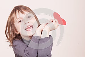 Funny portrait of cute little child girl holding red heart as symbol of love and amorousness