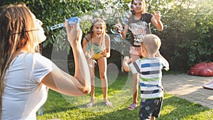 Funny portrait of happy cheerful young family blowing and cathcing soap bubbles at house backyard garden