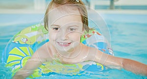 Funny portrait of happy cute little child girl playing with colorful ring in swimming pool