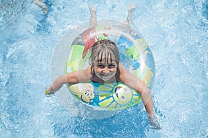 Funny portrait of happy cute little child girl playing with colorful ring in swimming pool. Kids learn to swim