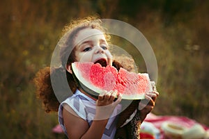 Funny portrait of an incredibly beautiful curly-haired little girl eating watermelon, healthy fruit snack, adorable toddler child