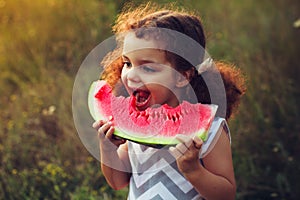 Funny portrait of an incredibly beautiful curly-haired little girl eating watermelon, healthy fruit snack, adorable toddler child