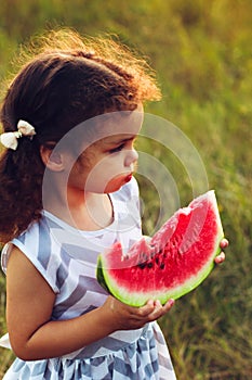 Funny portrait of an incredibly beautiful curly-haired little girl eating watermelon, healthy fruit snack, adorable toddler child