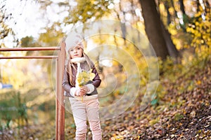 Funny portrait of a little girl. Little girl in a pink hat on a walk in the fall. Child girl in a jacket happily runs and collects