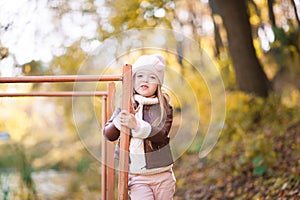 Funny portrait of a little girl. Little girl in a pink hat on a walk in the fall. Child girl in a jacket happily runs and collects
