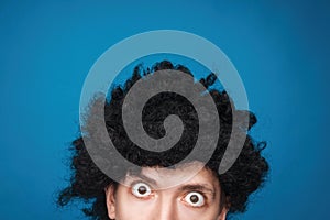 Funny portrait of a man with happy emotion on his face in the studio on blue background. Man wearing wig. Black hair