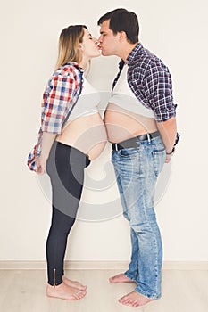 Funny portrait of pregnant couple standing face to face and kiss