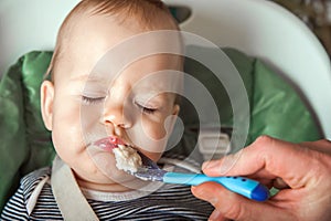 Funny portrait of toddler eating close-up. Complementary feeding of child with porridge at 9 months. Zucchini, cauliflower, brocco