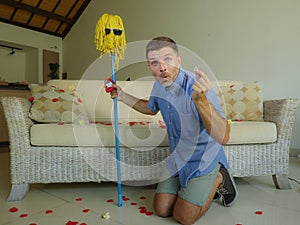 Funny portrait of young weird crazy and happy man holding mop with sunglasses as if it was his fiance kneeling and proposing marri