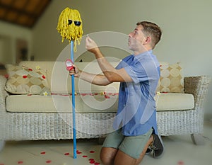 Funny portrait of young weird crazy and happy man holding mop with sunglasses as if it was his fiance kneeling and proposing marri