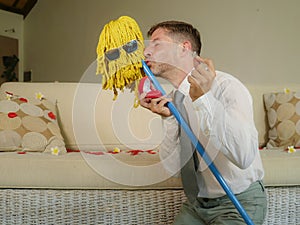 Funny portrait of young weird crazy and happy man holding mop with sunglasses as if it was his fiance kneeling and proposing marri