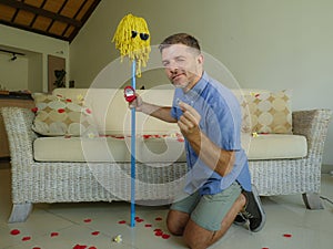 Funny portrait of young weird crazy and happy man holding mop with sunglasses as if it was his fiance kneeling and proposing marri