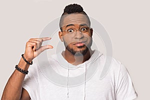 Funny positive African American man showing small size by fingers