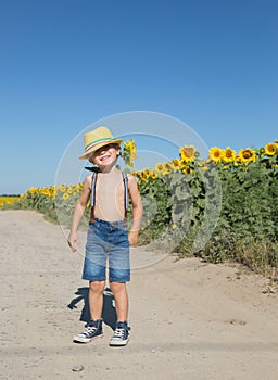 Funny positive boy of 4-5 years old in a yellow hat and shorts on suspenders with one sunflower
