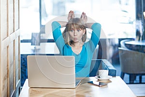 Funny positive childish woman working on laptop, having video call, showing bunny ears with hands.