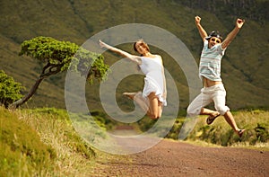 Jumping happy young couple in honneymoon. Just married jumping on countriside road. Background of lush green hills photo