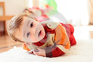 Funny and pretty baby girl smiles at her parents as she rolls on the floor at home