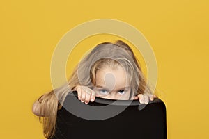 Funny and pretty child girl with long fair hair peeks out from behind a chair