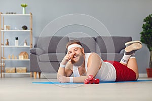 Funny red fat man doing exercises on the floor smiling while lying on the floor at home.