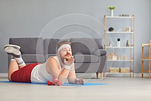 Funny red fat man doing exercises on the floor smiling while lying on the floor at home.