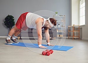 Funny red fat man doing exercises on the floor while standing at home.