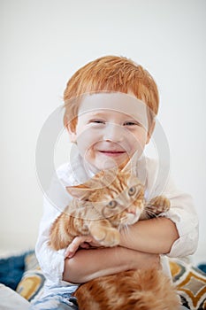 Funny red-haired boy in bed with a red cat