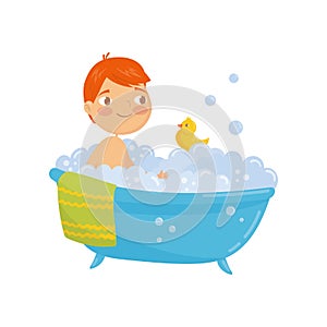 Funny red-haired boy taking bath with rubber duck toy. Bathtub with foam bubbles inside. Daily hygiene. Cartoon