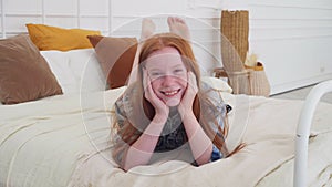 Funny red-haired girl with freckles smiling on bed