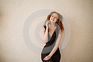 Funny red-haired woman posing in the background. Happy girl with facial expressions, black jumpsuit, curly