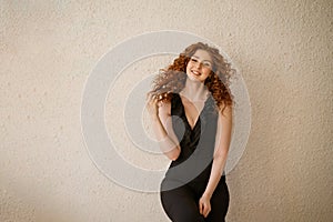 Funny red-haired woman posing in the background. Happy girl with facial expressions, black jumpsuit, curly .