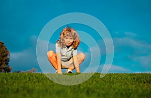 Funny redhead boy playing on the green grass in park, happy childhood. Kids active lifestyle outdoors.