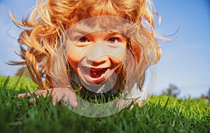 Funny redhead boy playing on the green grass in park, happy childhood. Kids active lifestyle outdoors. Funny excited kid