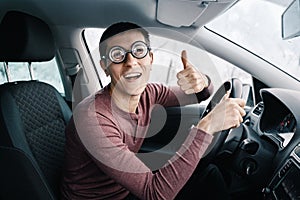Ridiculous idiotic nerd driver in big eyeglasses holding the steering wheel and smiling to the camera. Concept of a
