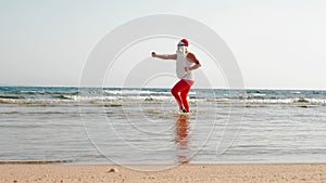 Funny Santa Claus. Father Christmas, in sunglasses and flippers, having fun in the sea water near sandy beach. Santa