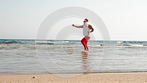 Funny Santa Claus. Father Christmas, in sunglasses and flippers, having fun in the sea water near sandy beach. Santa