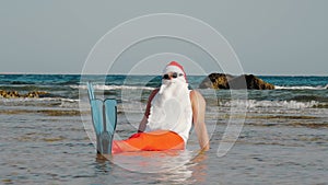 Funny Santa Claus. Father Christmas, in sunglasses and flippers, sitting and having fun, relaxing in the sea water near